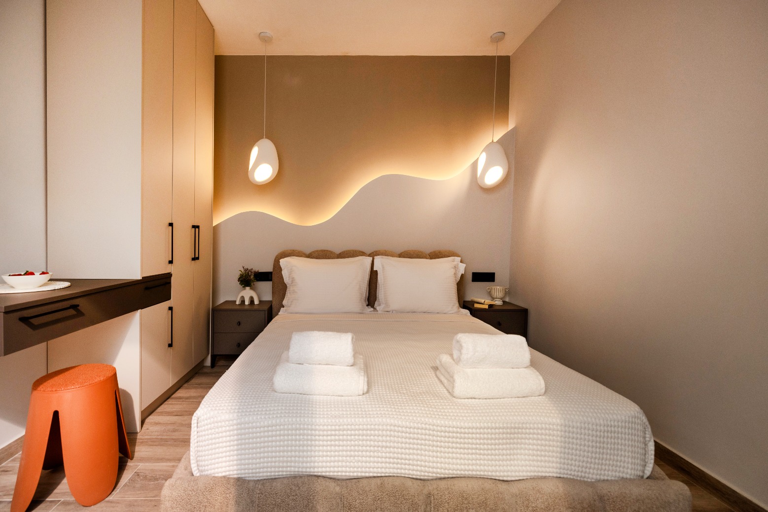 Modern hotel bedroom with white bedding, wave-shaped backlit wall, pendant lamps, built-in wardrobe, nightstands.