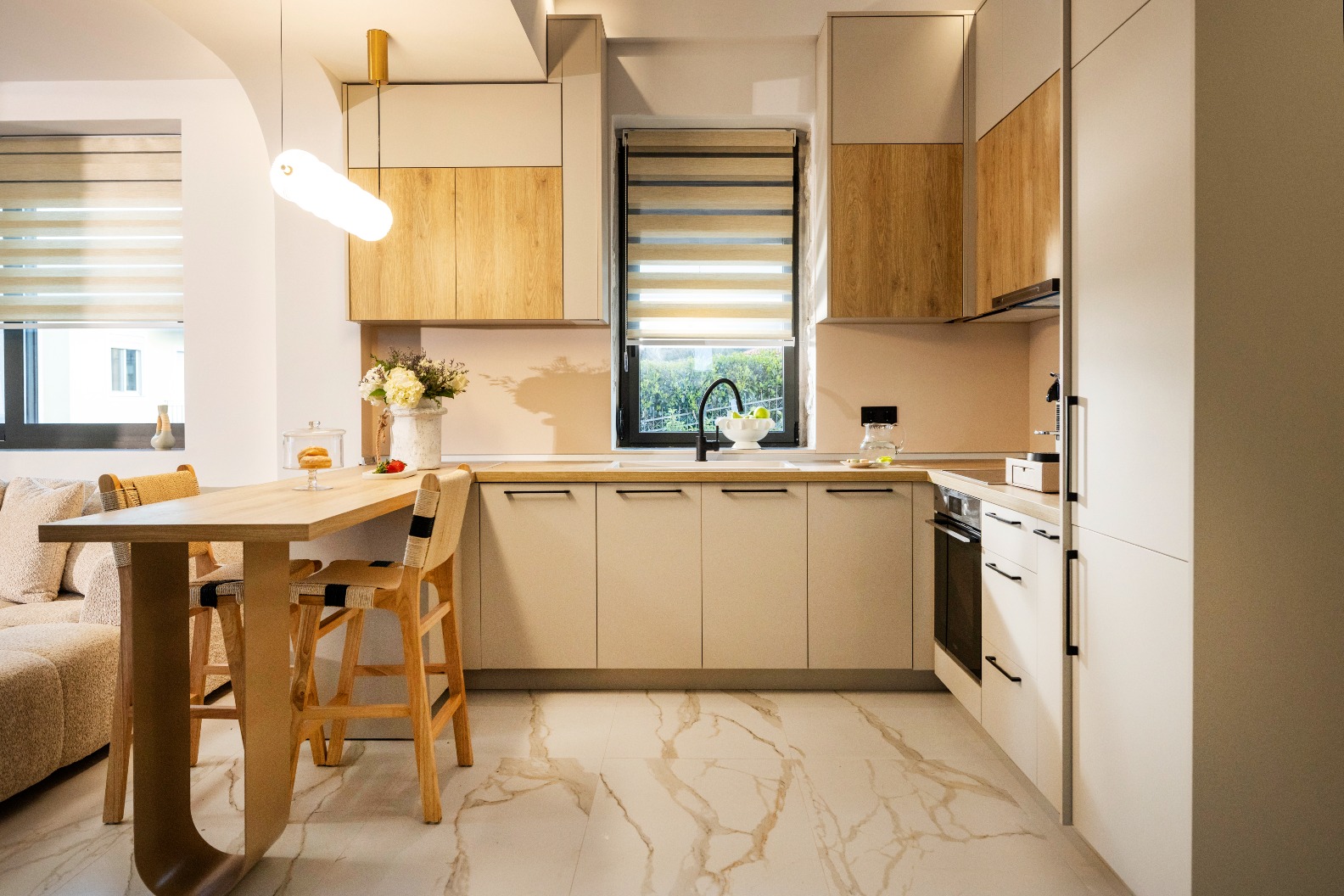 Modern kitchen with light wood cabinets, marble floors, window blinds, and a wooden dining table with chairs.