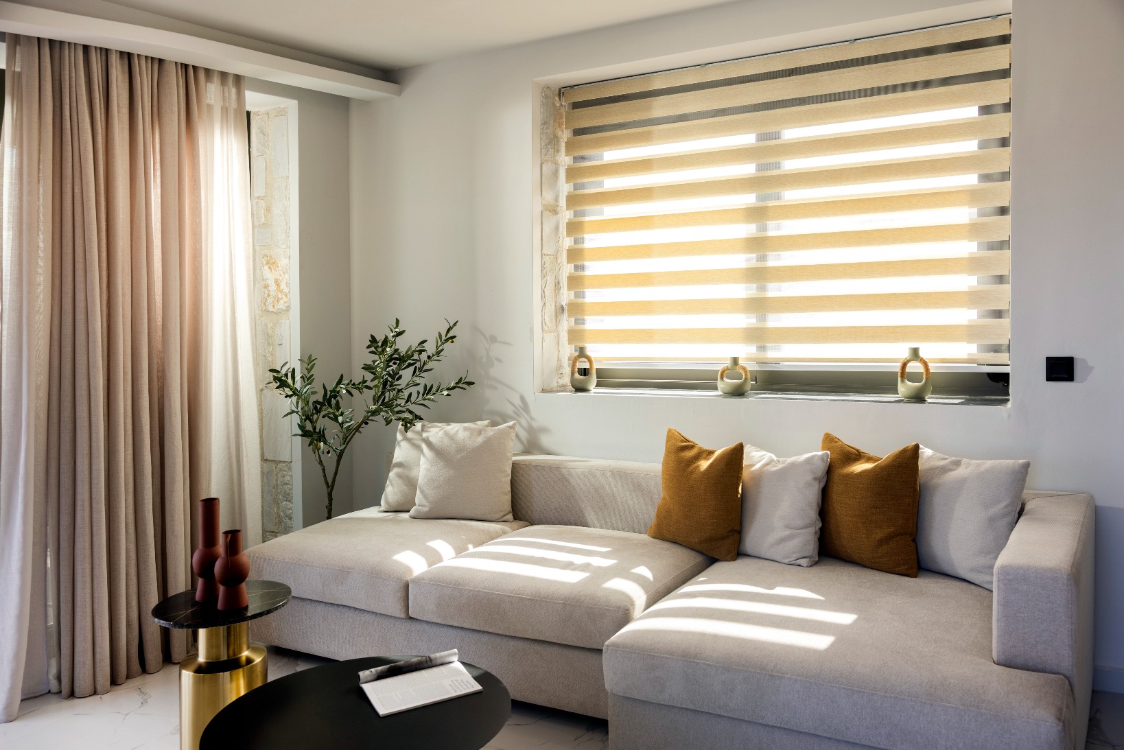 Bright modern living room with beige sectional, striped roller blinds, soft curtains, and mustard throw pillows.