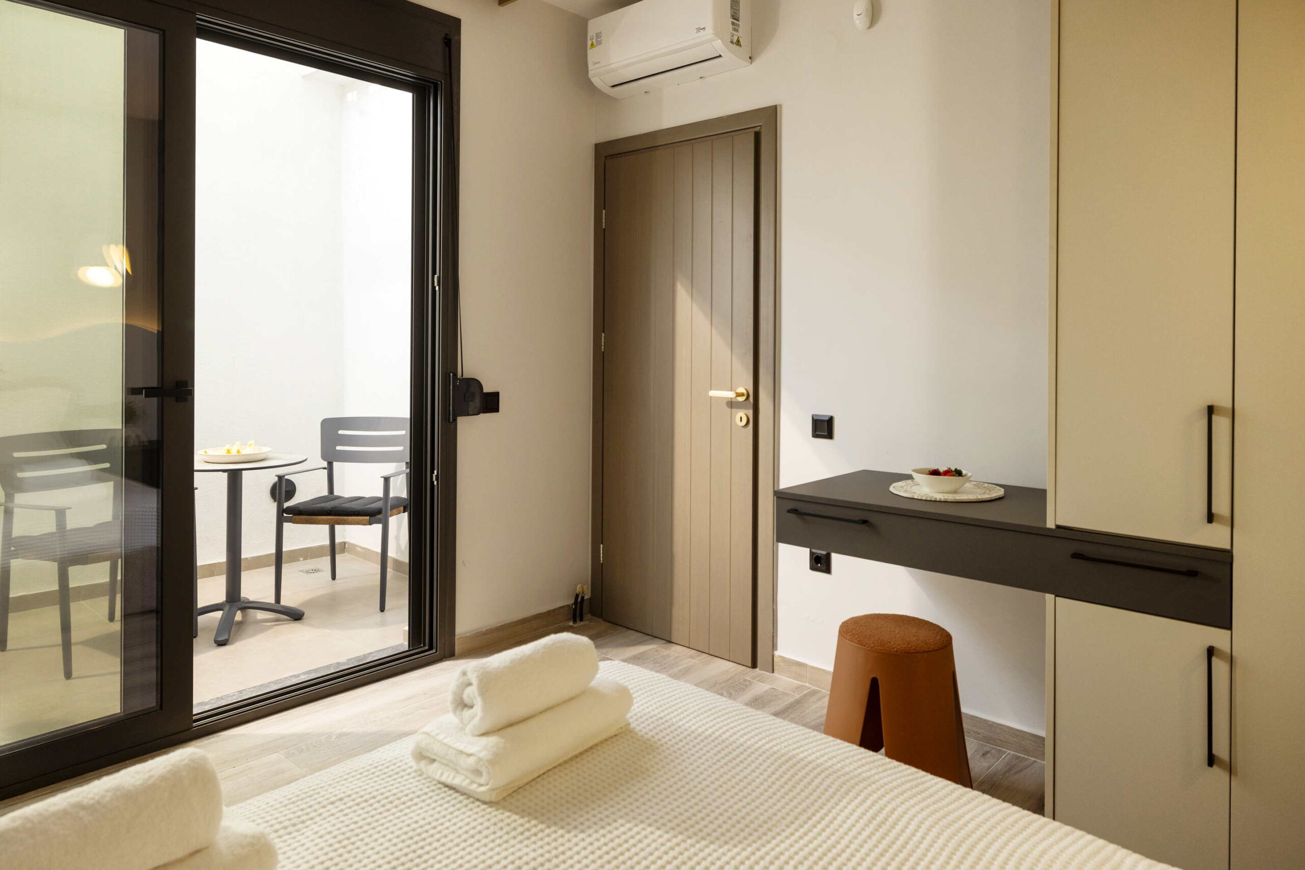 Modern hotel room with balcony access via sliding glass door, desk, and neatly folded towels on the bed.