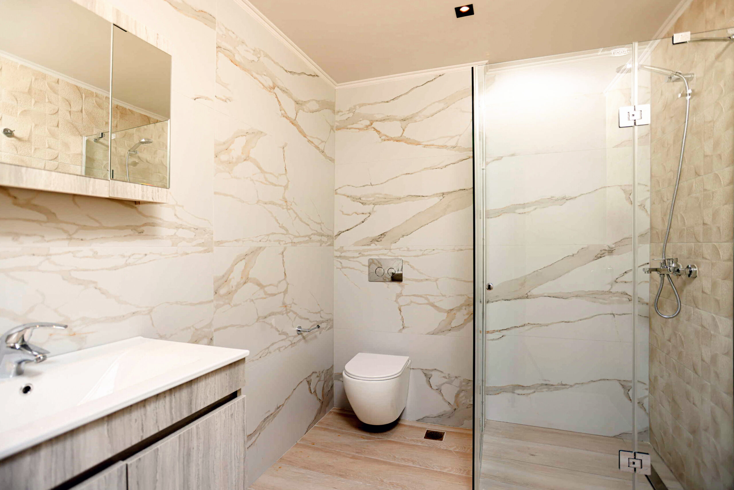 Modern marble-tiled bathroom with glass shower enclosure, wall-mounted vanity, and wall-hung toilet.