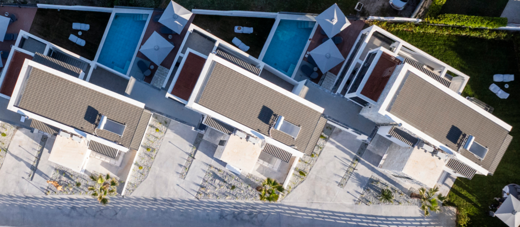 Aerial view of modern apartment complex with blue pools, white buildings, and sun loungers.