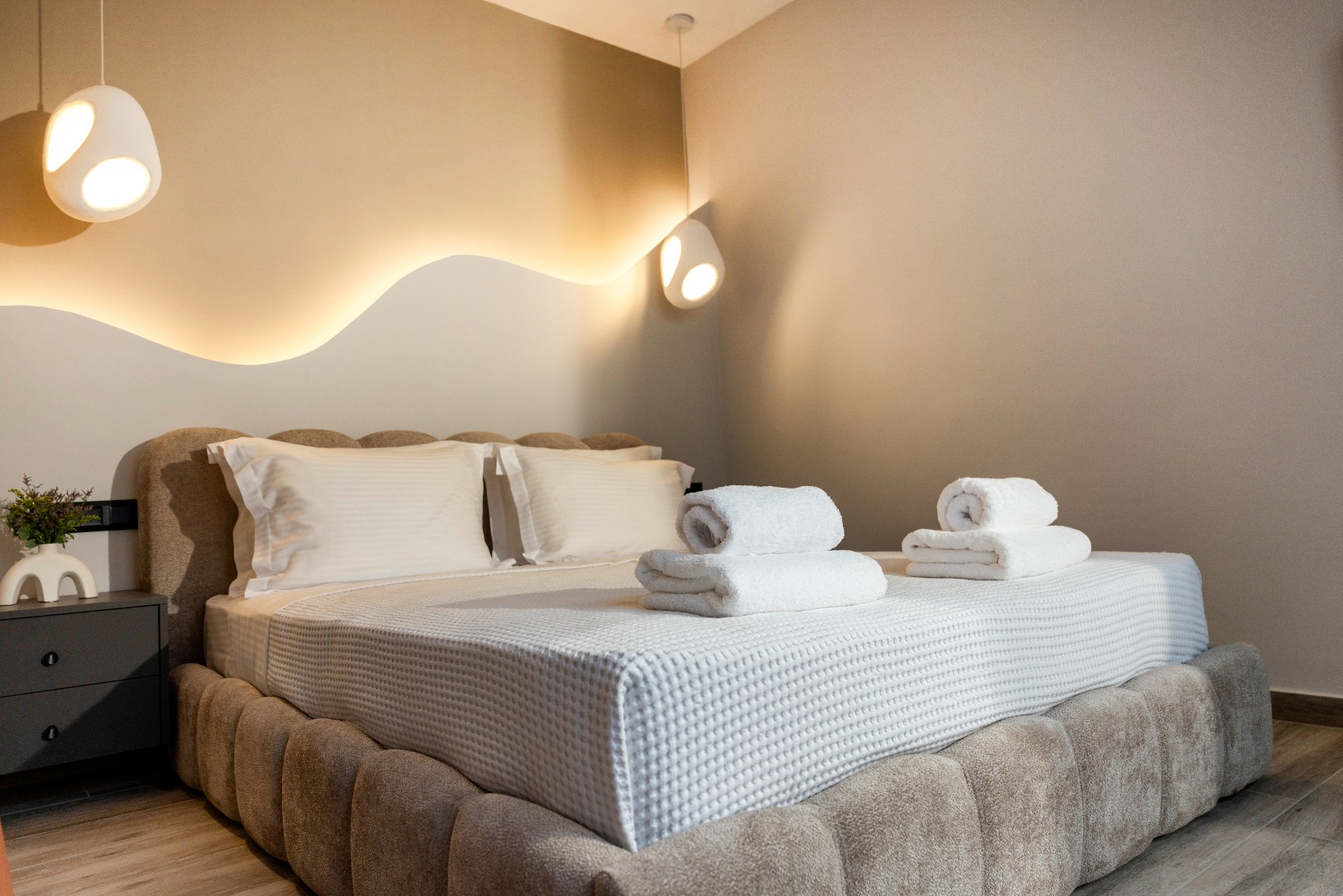 Modern hotel-style bedroom with tufted platform bed, warm ambient lighting, white bedding, and folded towels.