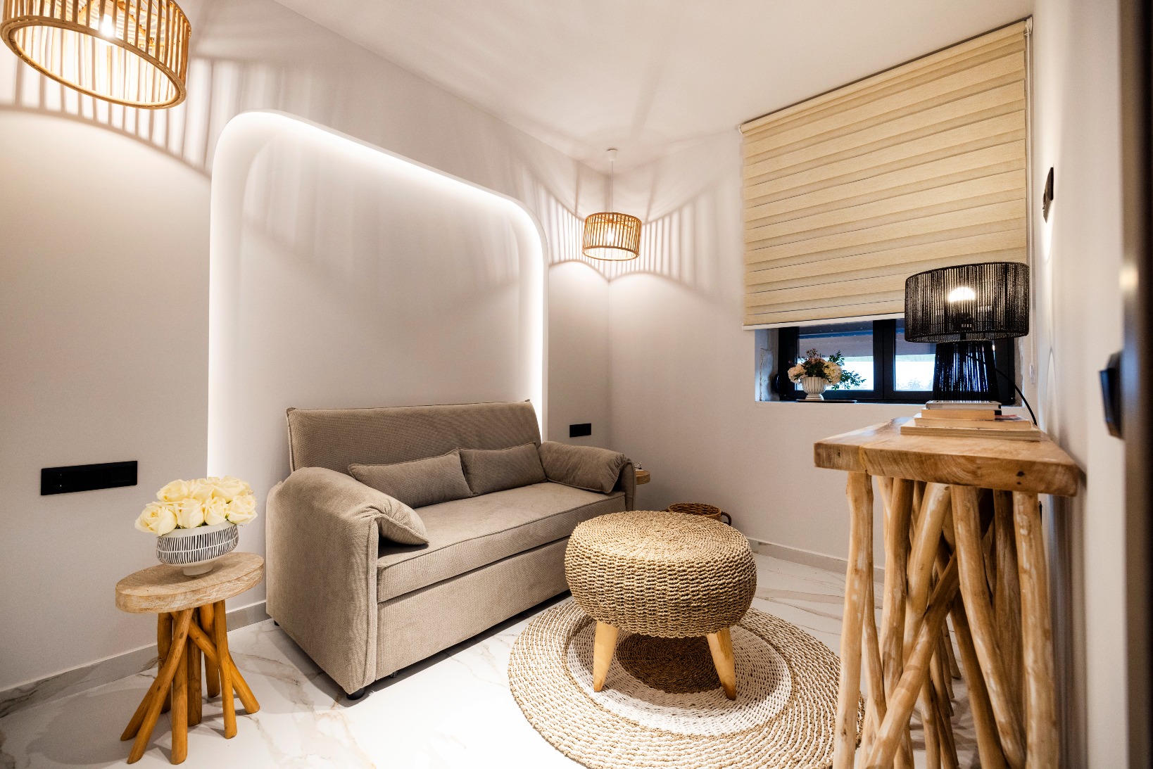 Cozy modern living room with beige sofa, round woven ottoman, and natural wood accents under warm lighting.