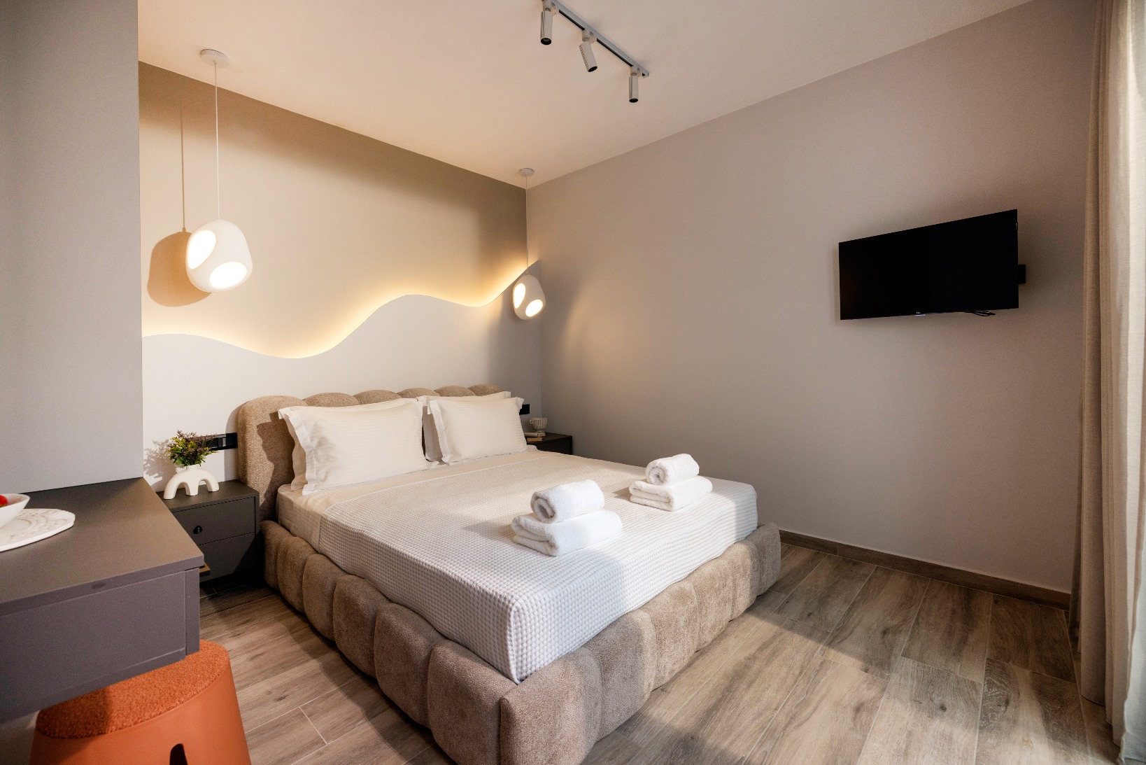 Modern hotel room with plush king bed, wave headboard lighting, wall-mounted TV, and chic decor.