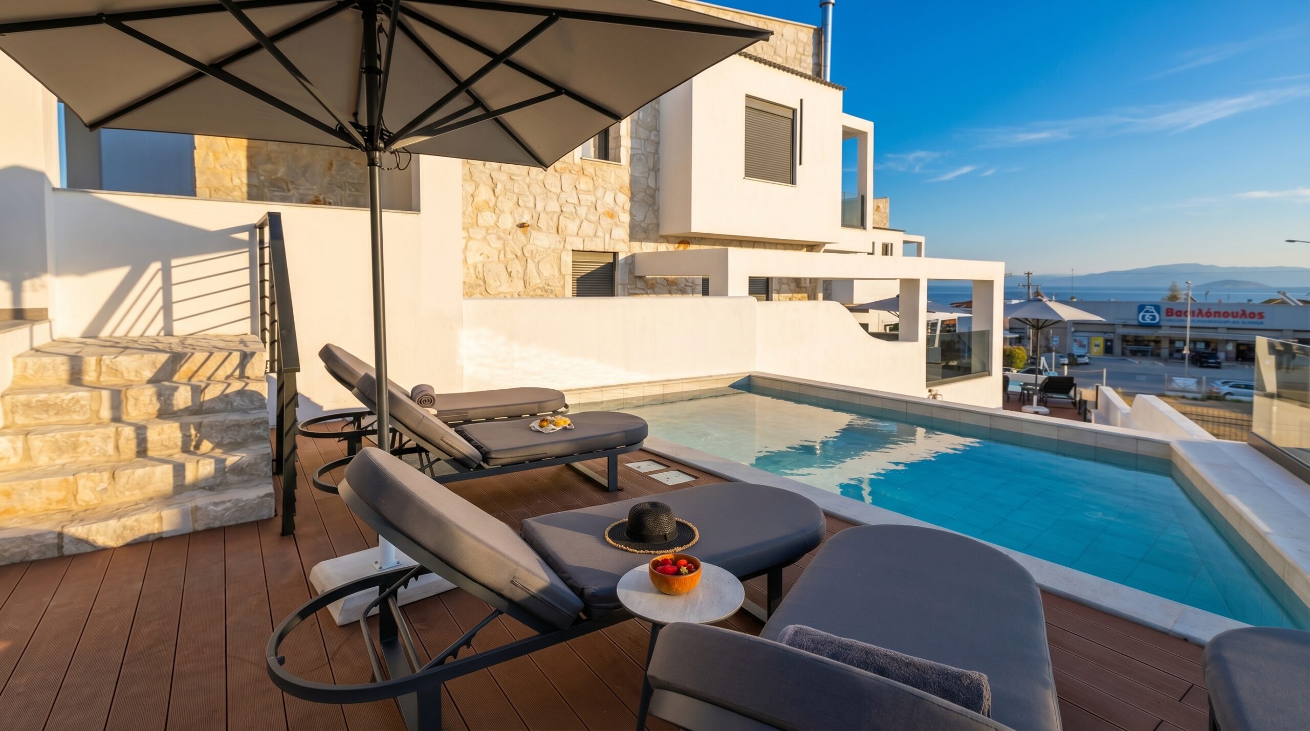 Modern hotel terrace with sun loungers, umbrella, and pool, white stone walls, and sea view.