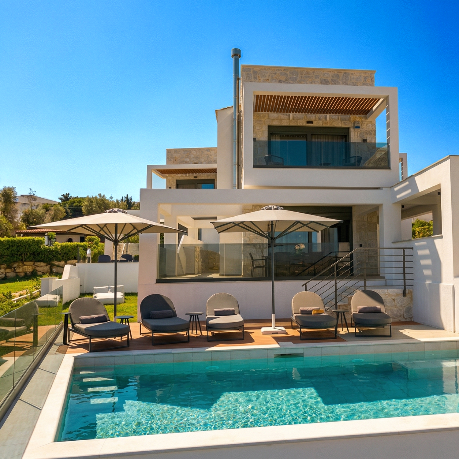 Modern luxury villa in Greece Halkidiki with stone facade, glass balcony, and poolside lounge chairs under blue sky.